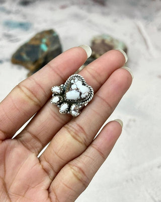 Silver ring with white stones held in a hand against a textured background