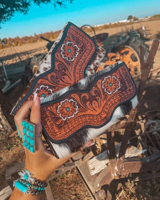 Decorative wallets with intricate patterns held by a hand in an outdoor setting.