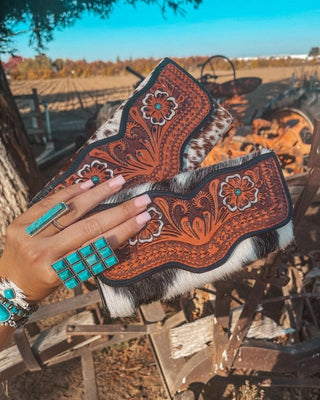 Decorative wallets with intricate patterns and turquoise accents, held by a hand in an outdoor setting.