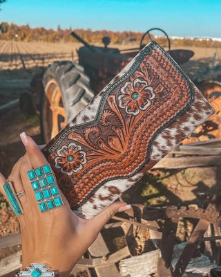 Hand holding a decorative clutch with intricate patterns and turquoise highlights, set against a rustic background.