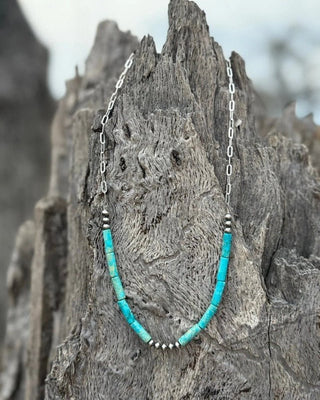 Turquoise beaded necklace with silver chain on a textured wooden surface