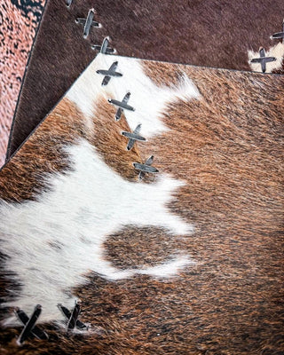 A close-up of a cowhide bowl with a brown and white natural pattern, stitched along the edge with dark metal grommets.