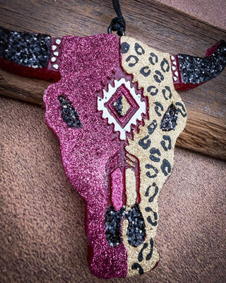 Maroon and leopard bull skull car freshie laying on wood