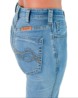 Close-up back view of a person wearing light blue denim jeans, showing the TUFF brand patch on the back pocket and decorative metallic stitching on the rear right pocket.
