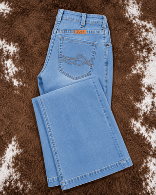 Light blue denim jeans laid flat on a brown and white cowhide rug, showing the back pocket with decorative stitching and a small orange 'Puff' brand tab.