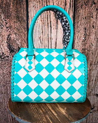 A turquoise and white checkered leather handbag with double top handles, displayed on a round wooden stool against a rustic wood plank background.