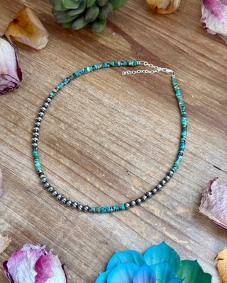 Necklace with blue and black beads on a wooden surface with flowers