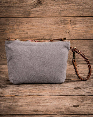 A gray fabric wristlet pouch with a brown leather wrist strap and zipper, displayed on a rustic wooden plank background.