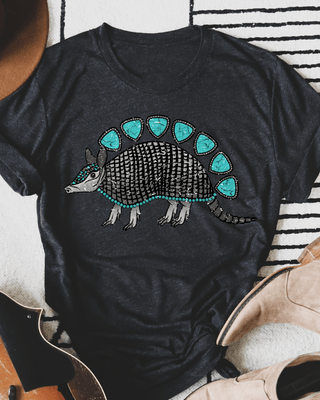 Black t-shirt with armadillo graphic on a striped surface with boots and a hat.