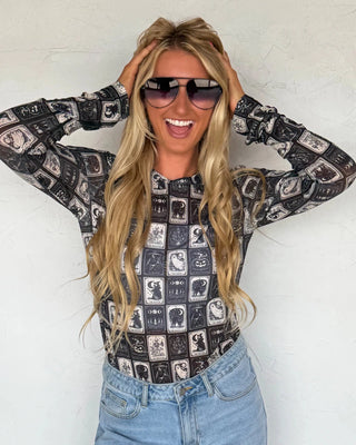 Woman wearing a patterned long-sleeve top and sunglasses against a white background