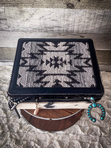 The Myra Bag - Mausoleum Jewelry Box sitting on a wooden wire wheel with jewelry hanging out of the opening. the table is on gray carpet.