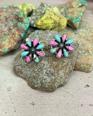 Flower-shaped earrings with pink and blue colors on a rock background