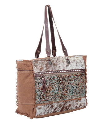 Brown tote bag with cowhide leather and intricate pattern on a white background