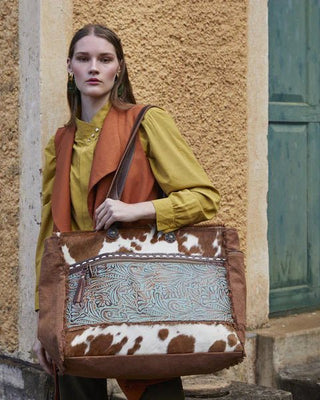 Woman holding a brown leather bag with cowhide pattern against a textured wall.