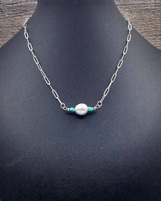 A silver paperclip chain necklace displayed on a black mannequin bust, featuring a central white pearl flanked by two small turquoise beads.
