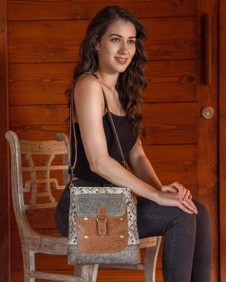 Woman sitting on a wooden chair holding a brown and gray handbag against a wooden background