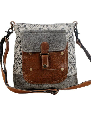 Crossbody bag with patterned fabric and brown leather flap on a white background