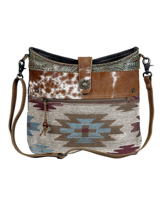 Multicolored patterned handbag with brown leather accents on a white background