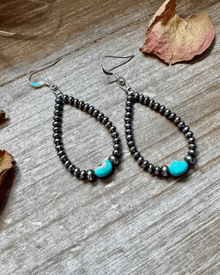 Silver beaded earrings with turquoise accents on a wooden surface with dried leaves.