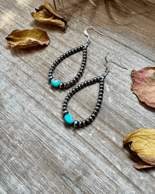 Beaded earrings with turquoise stones on a wooden surface with dried leaves.