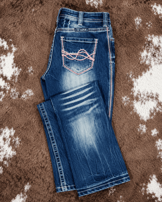 A pair of blue denim jeans with a front pocket featuring a pink embroidered wave design, laid flat on a brown and white cowhide rug. The brand name 'TUFF' is visible on the back waistband.