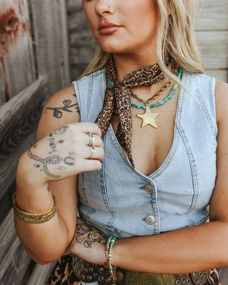 Woman wearing a denim vest, leopard print pants, and multiple necklaces with a star pendant.
