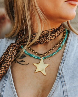 Close-up of a person wearing a leopard print scarf, gold star necklace, and denim jacket.