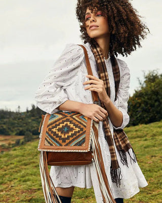 Woman holding a patterned handbag with fringes in an outdoor setting