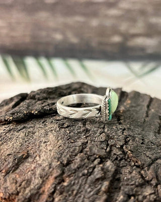 A sterling silver ring with a textured geometric band and a green oval stone, resting on a piece of dark wood.