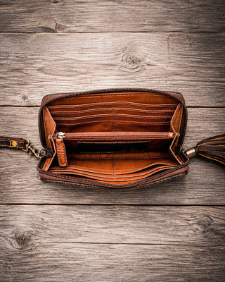 An open brown leather zip-around wallet or clutch with multiple card slots and an interior pocket, photographed from above on a rustic gray-brown wooden plank surface.
