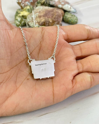 Silver necklace with a small pendant held in a hand, with rocks in the background.
