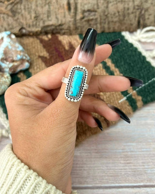 Hand wearing a turquoise ring with a textured background