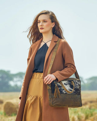 Woman in a brown coat holding a patterned handbag in an outdoor setting