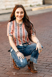 Woman modeling peach and navy aztec top on a brick street.