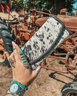Hand holding a cowhide wallet with a rustic background of old tractors.