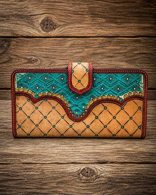 A handcrafted long wallet made of tan leather with turquoise blue geometric patterns, red stitching, and gold accents, displayed on a rustic wooden background.