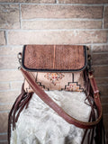 Front view of the Sandy Rosewood Hand-Tooled Bag on a blanket in front of a brick wall.