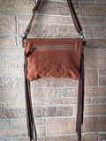 Back view of the Sandy Rosewood Hand-Tooled Bag hanging on a brick wall.